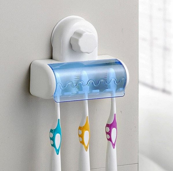 Wall-mounted toothbrush holder with three colorful toothbrushes on a light gray wall.