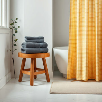 Bathroom with gray towels on a wooden stool, white bathtub, and yellow plaid shower curtain with a beige bathmat