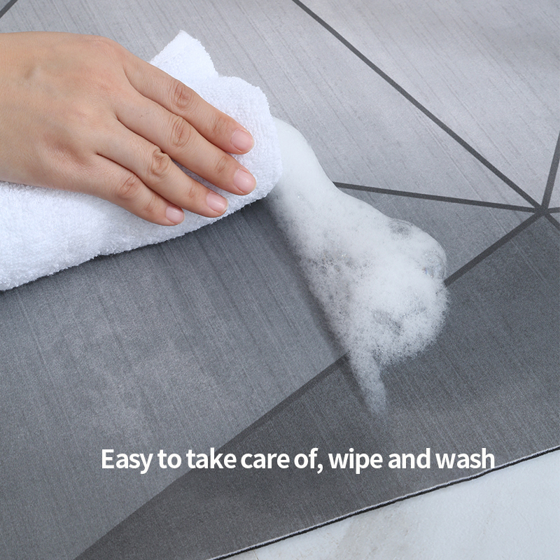 Hand using a white cloth to wipe a gray surface of a geometric bathmat with text 'Easy to take care of, wipe and wash'.